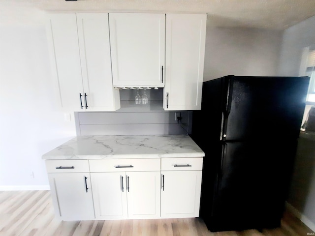 kitchen with black refrigerator, light stone counters, white cabinetry, and light hardwood / wood-style floors