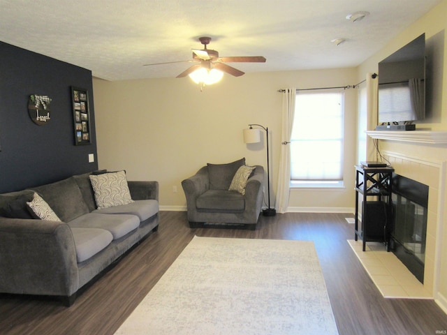 living room with dark wood-type flooring, ceiling fan, and a tile fireplace