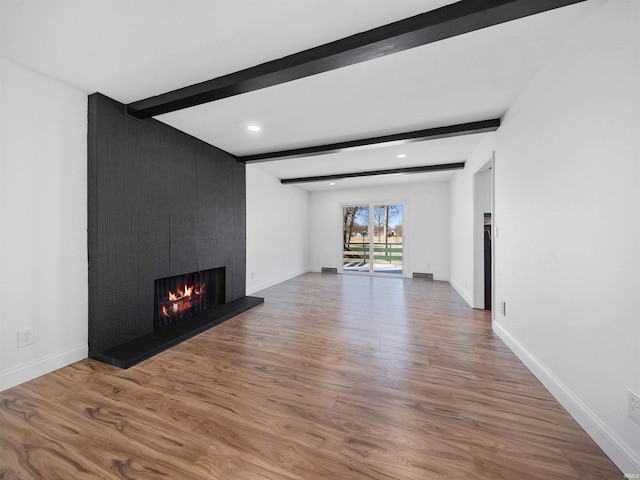 unfurnished living room featuring hardwood / wood-style flooring, a large fireplace, and beamed ceiling