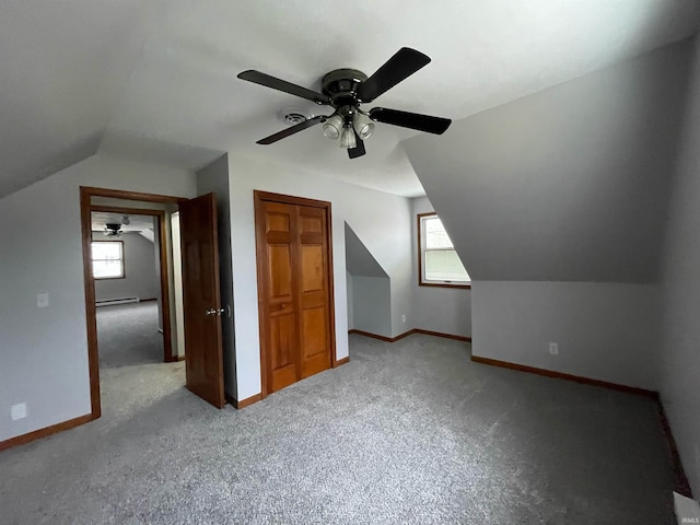 additional living space with light colored carpet, a healthy amount of sunlight, vaulted ceiling, and a baseboard heating unit