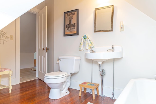 bathroom with a tub to relax in, hardwood / wood-style floors, and toilet