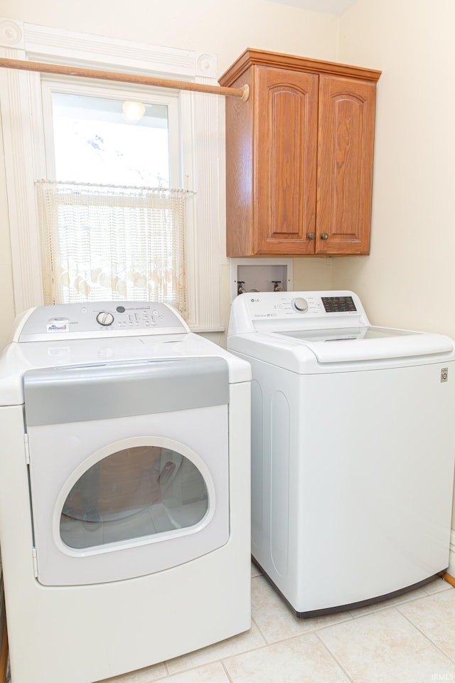 washroom featuring washing machine and dryer, cabinets, and light tile patterned flooring