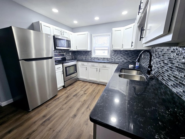 kitchen featuring hardwood / wood-style floors, white cabinetry, sink, dark stone countertops, and stainless steel appliances