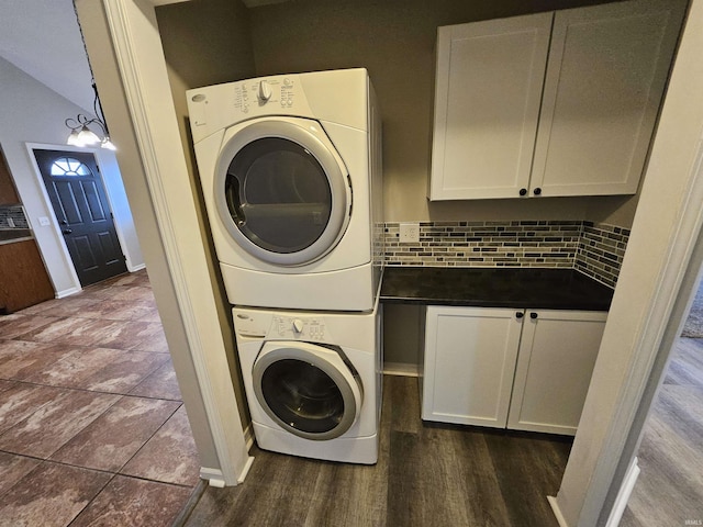 washroom featuring stacked washer / dryer, dark wood-type flooring, and cabinets