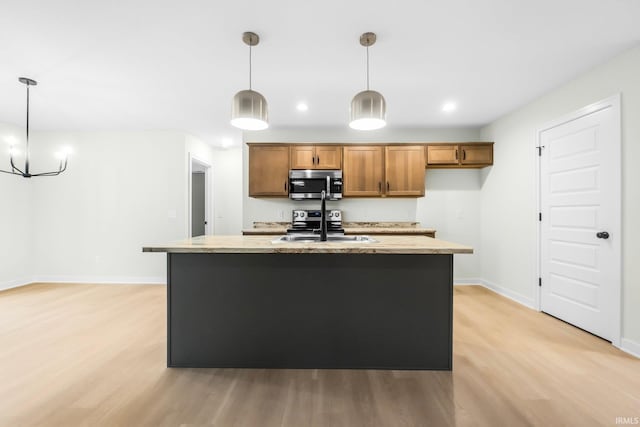 kitchen with sink, light stone counters, hanging light fixtures, light hardwood / wood-style flooring, and a kitchen island with sink