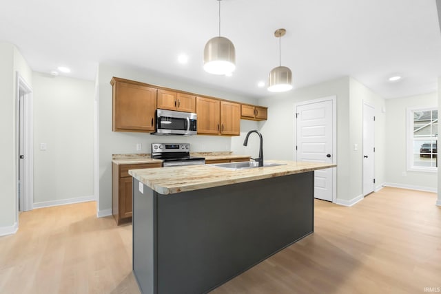 kitchen with sink, a kitchen island with sink, hanging light fixtures, stainless steel appliances, and light wood-type flooring