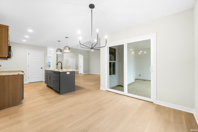 kitchen with sink, hanging light fixtures, black dishwasher, an island with sink, and light hardwood / wood-style floors