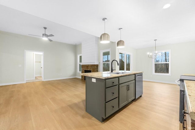 kitchen featuring an island with sink, sink, gray cabinetry, stainless steel dishwasher, and light stone countertops