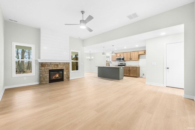 unfurnished living room with sink, ceiling fan with notable chandelier, a fireplace, and light hardwood / wood-style floors