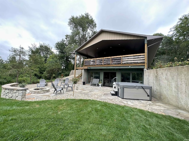 rear view of property with a fire pit, a wooden deck, a yard, a hot tub, and a patio area