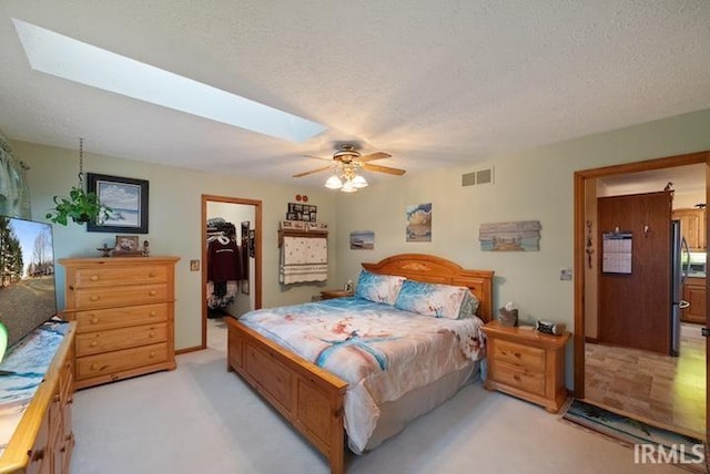 carpeted bedroom featuring a walk in closet, stainless steel fridge, a skylight, and a textured ceiling