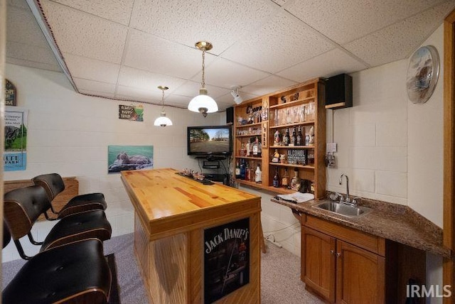 bar featuring a paneled ceiling, wooden counters, decorative light fixtures, and sink