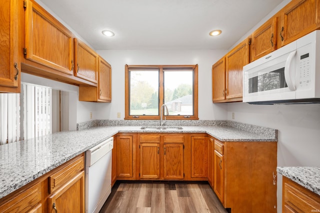 kitchen with sink, white appliances, light hardwood / wood-style flooring, light stone countertops, and kitchen peninsula