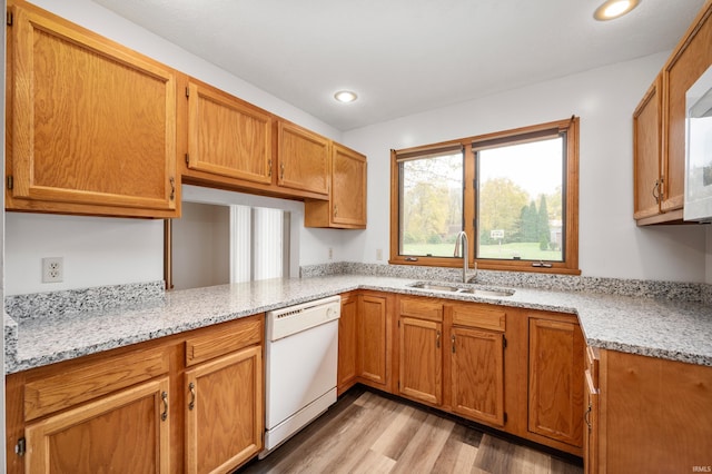 kitchen with white dishwasher, sink, light hardwood / wood-style flooring, and light stone countertops