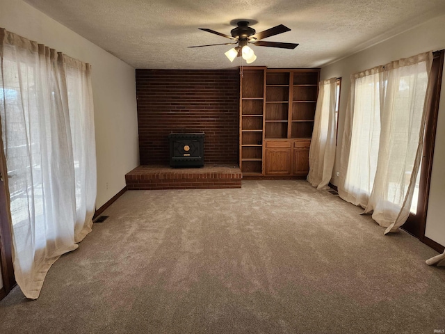 unfurnished living room featuring ceiling fan, a wood stove, light carpet, and a textured ceiling