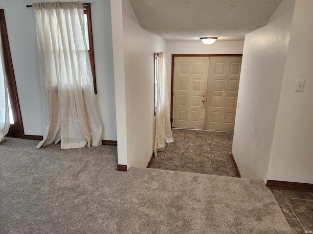 hall featuring a textured ceiling and dark colored carpet