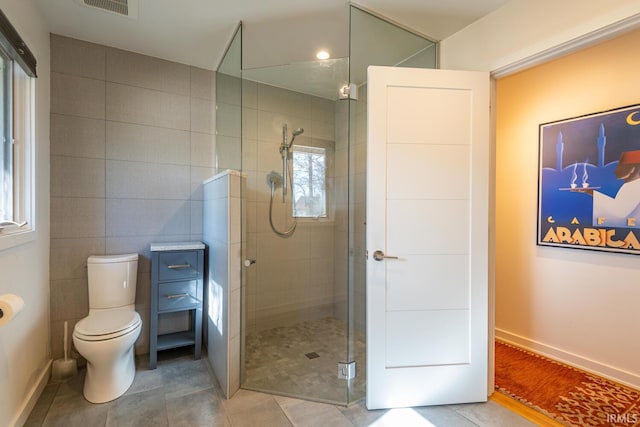 bathroom with walk in shower, tile patterned floors, toilet, and tile walls