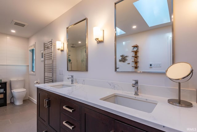 bathroom with tile patterned flooring, tile walls, a skylight, vanity, and toilet