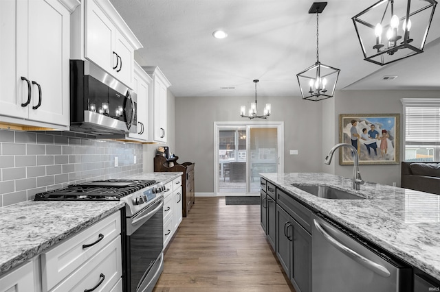 kitchen featuring sink, appliances with stainless steel finishes, hanging light fixtures, light stone counters, and white cabinets