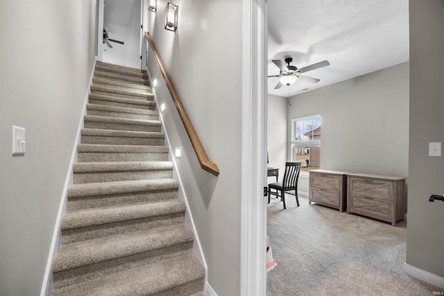 stairway with a textured ceiling, carpet floors, and ceiling fan