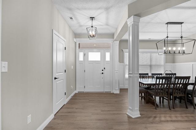 foyer entrance featuring wood-type flooring, decorative columns, a textured ceiling, and a notable chandelier