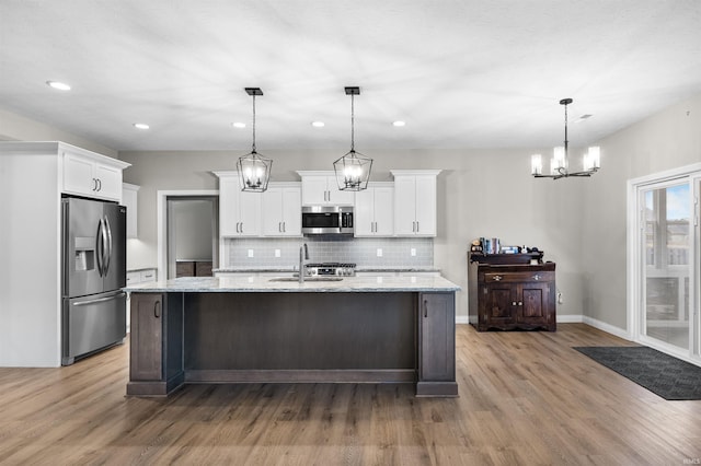 kitchen with hanging light fixtures, stainless steel appliances, white cabinets, and light stone countertops