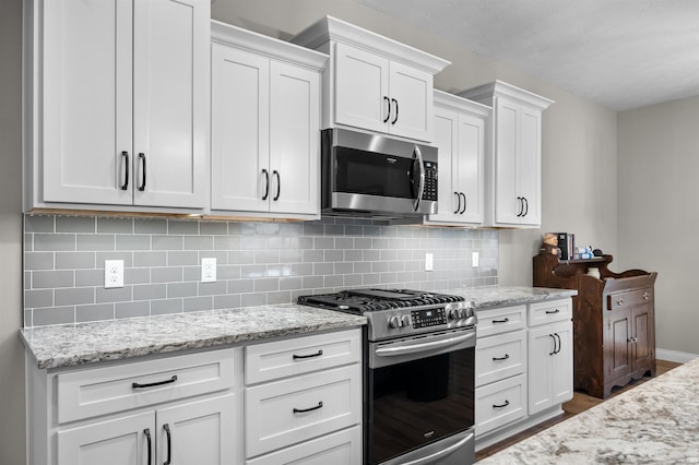 kitchen with white cabinetry, stainless steel appliances, light stone countertops, and tasteful backsplash