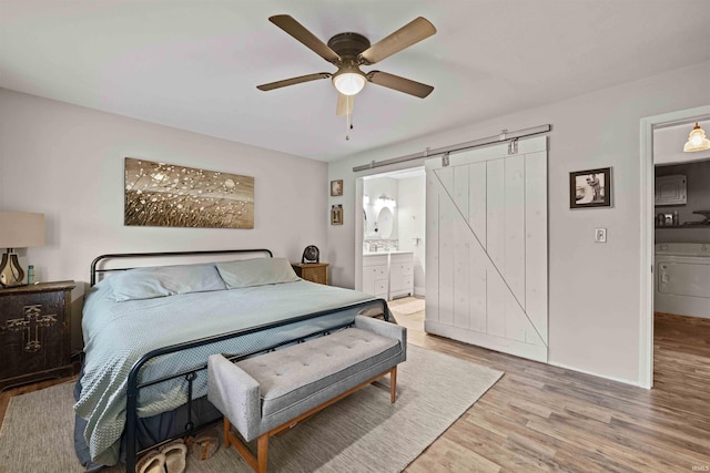 bedroom with ceiling fan, connected bathroom, wood-type flooring, washer / clothes dryer, and a barn door