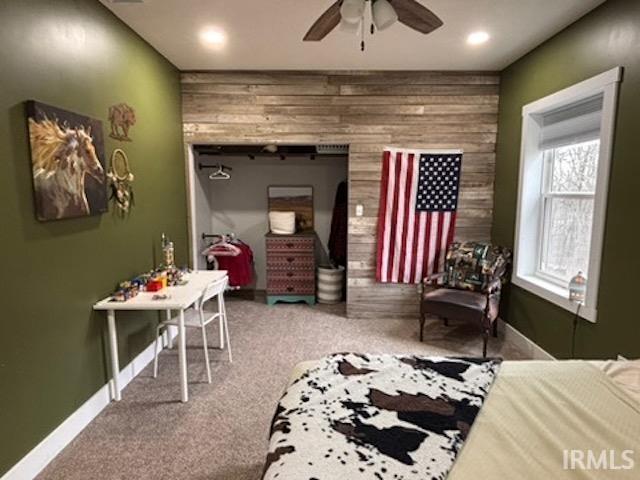 bedroom with ceiling fan, wooden walls, and carpet floors