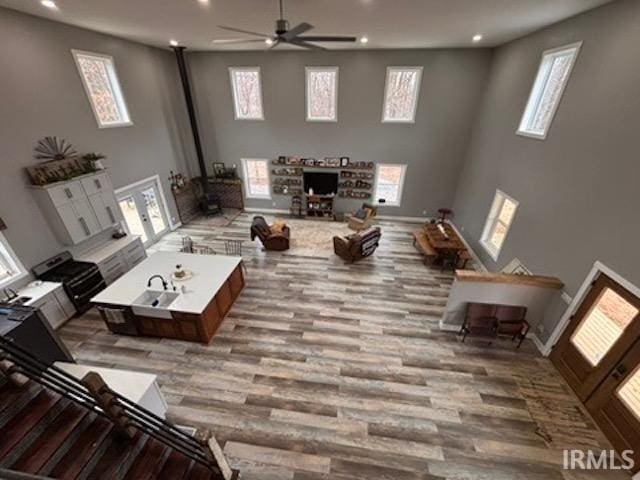 living room featuring a wood stove, a high ceiling, ceiling fan, light hardwood / wood-style floors, and french doors