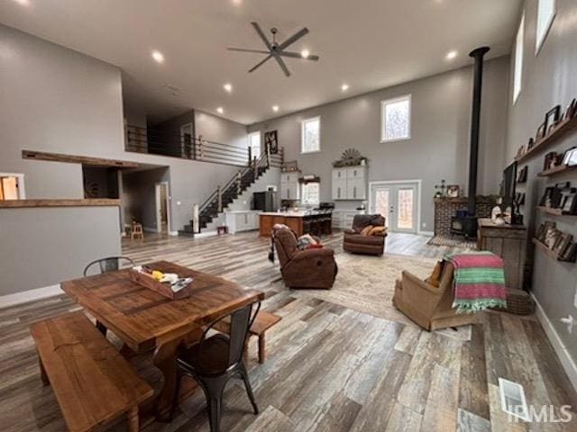 living room with ceiling fan, a wood stove, light wood-type flooring, and a towering ceiling