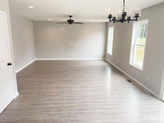 spare room with wood-type flooring and ceiling fan with notable chandelier