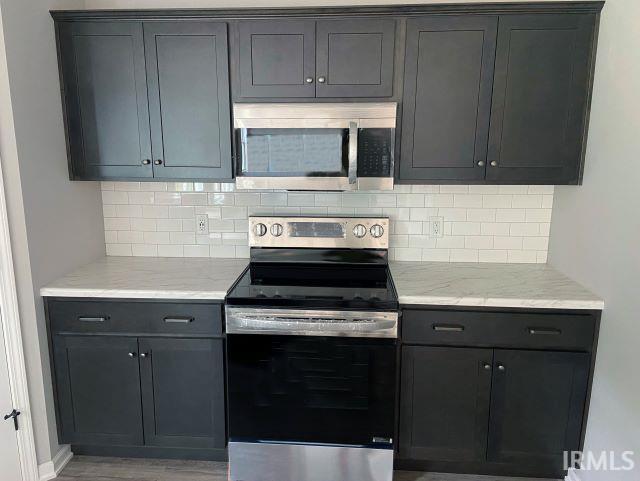 kitchen featuring light stone counters, tasteful backsplash, stainless steel appliances, and light wood-type flooring