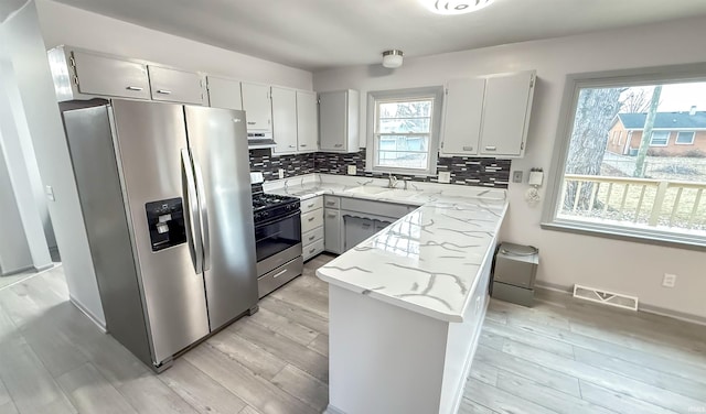 kitchen featuring sink, decorative backsplash, light stone counters, stainless steel appliances, and light wood-type flooring