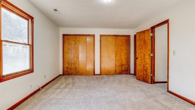 unfurnished bedroom with multiple windows, multiple closets, and light colored carpet