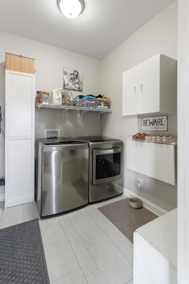 clothes washing area with cabinets, washing machine and clothes dryer, and a textured ceiling