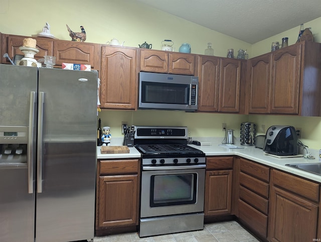 kitchen with appliances with stainless steel finishes, sink, vaulted ceiling, and a textured ceiling