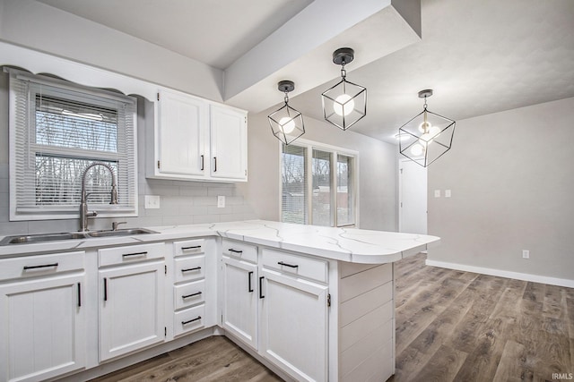 kitchen with decorative light fixtures, white cabinetry, wood-type flooring, sink, and kitchen peninsula