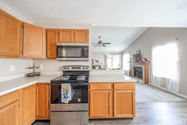 kitchen featuring vaulted ceiling, light wood-type flooring, ceiling fan, stainless steel appliances, and a fireplace