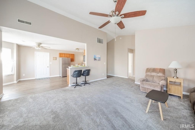 living area with ceiling fan, vaulted ceiling, and light carpet