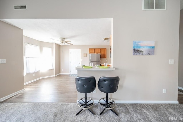 kitchen featuring a breakfast bar, light carpet, stainless steel fridge, and ceiling fan