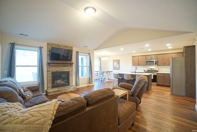 living room with lofted ceiling, a stone fireplace, hardwood / wood-style floors, and a notable chandelier