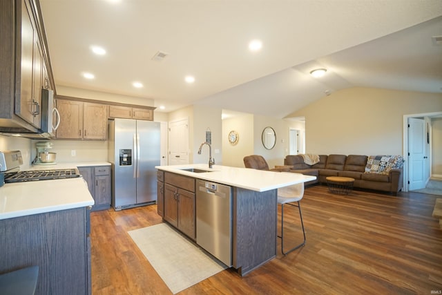 kitchen with vaulted ceiling, appliances with stainless steel finishes, sink, dark hardwood / wood-style flooring, and a center island with sink