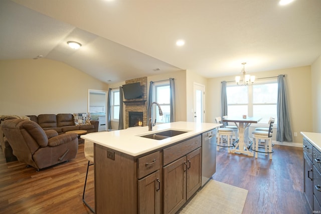 kitchen featuring pendant lighting, sink, a large fireplace, stainless steel dishwasher, and a center island with sink