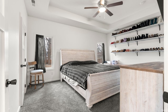 bedroom featuring dark carpet, a tray ceiling, and ceiling fan