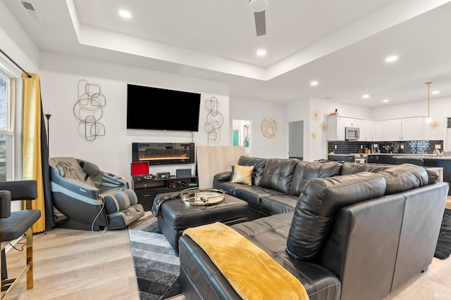 living room featuring ceiling fan, a raised ceiling, and light hardwood / wood-style floors