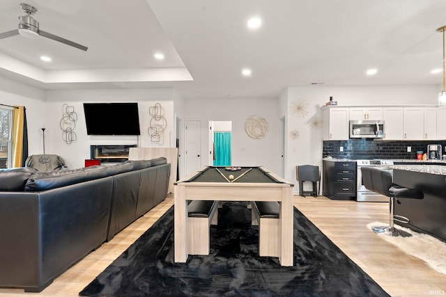 game room featuring a raised ceiling, ceiling fan, light wood-type flooring, and billiards