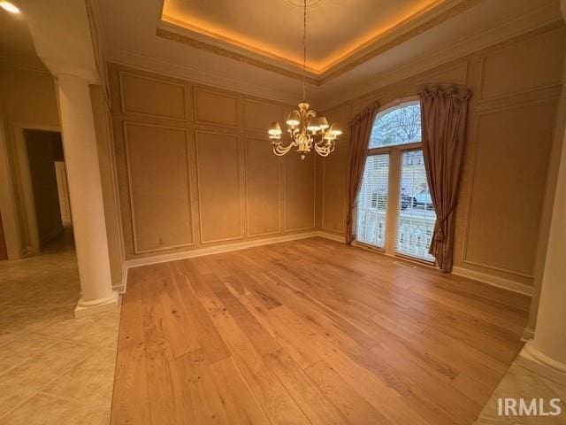 unfurnished room featuring crown molding, an inviting chandelier, a tray ceiling, light hardwood / wood-style floors, and ornate columns