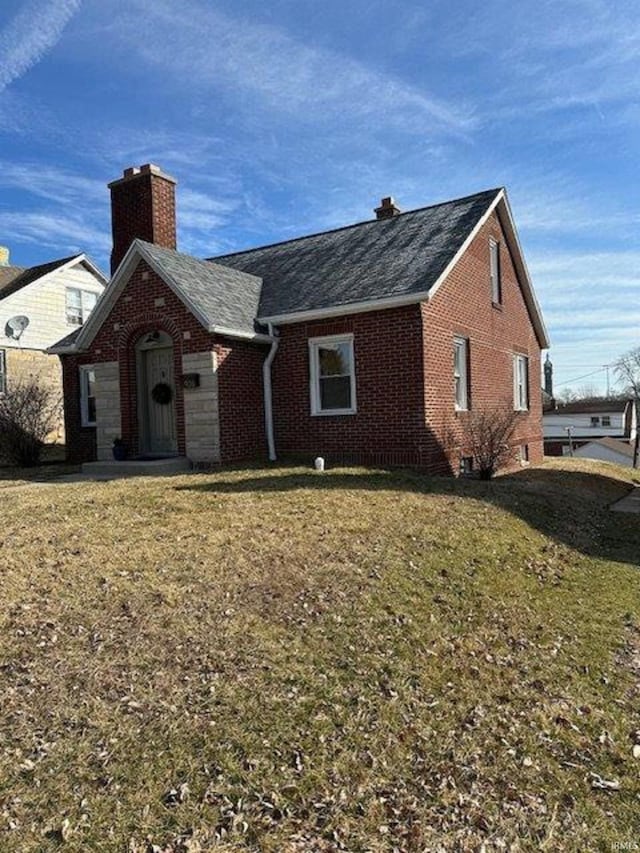 view of front facade with a front yard, brick siding, and a chimney