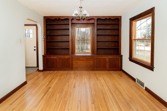 unfurnished dining area featuring a chandelier, built in features, and light wood-type flooring